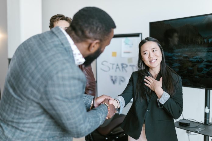 man shaking womans hand thanking her with colleague looking on