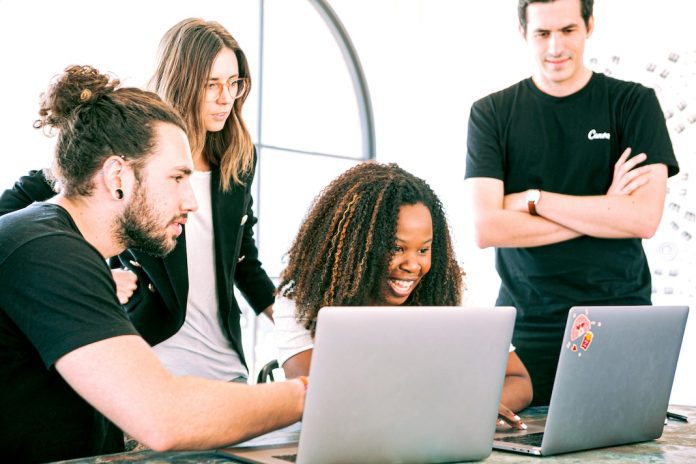 A Group of smiling Professionals huddled around laptops Sharing Ideas